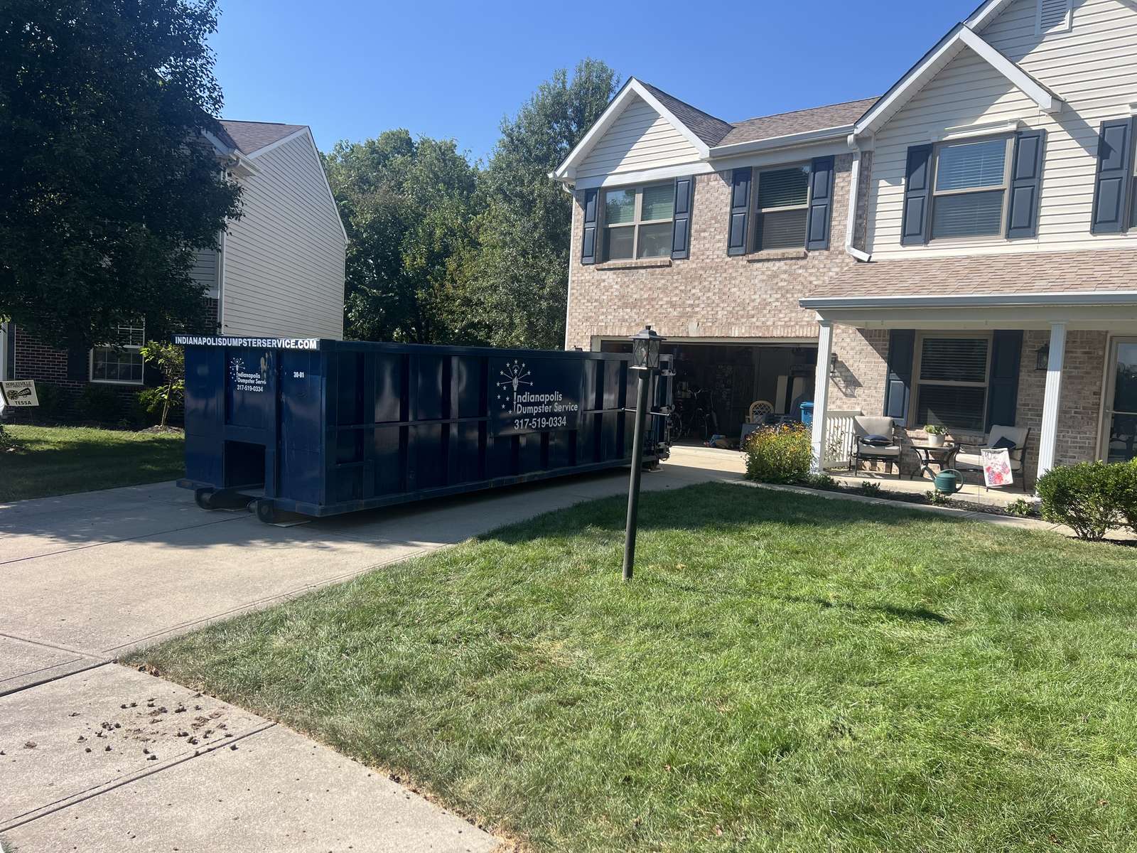 A navy Indianapolis Dumpster Service roll off container in Noblesville. On a concrete driveway, door end facing the garage.