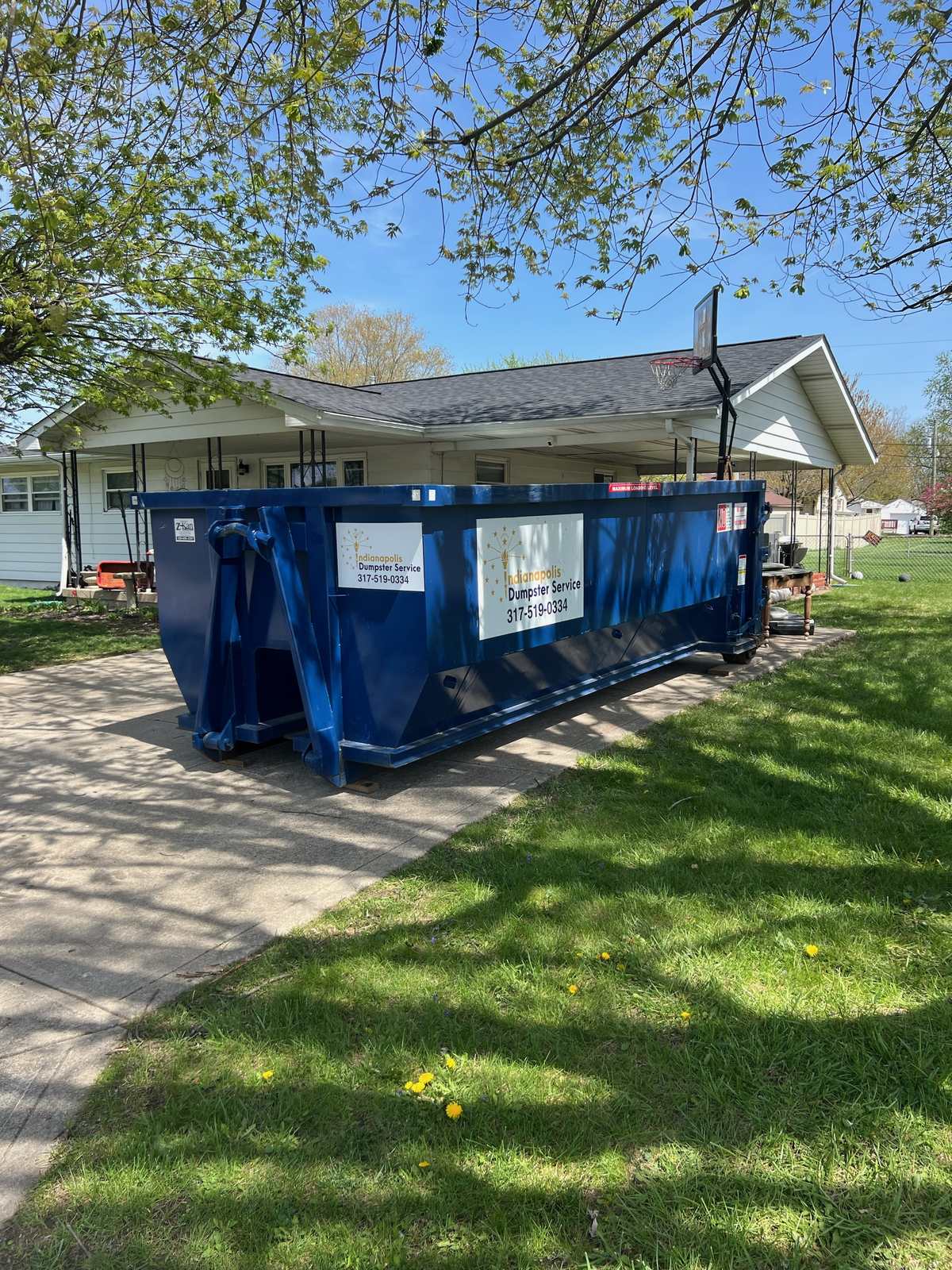 A navy Indianapolis Dumpster Service roll off container in Pittsboro. On the grass beside a ranch home's driveway.