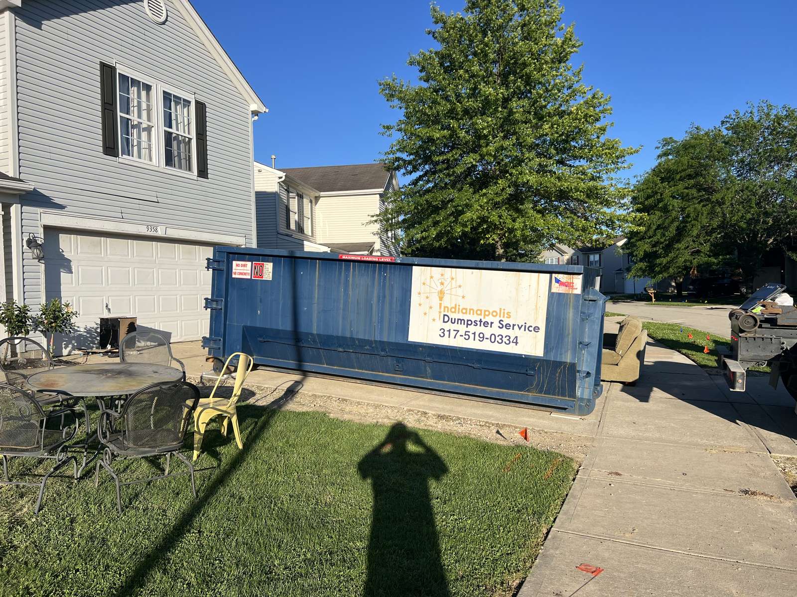 A navy Indianapolis Dumpster Service roll off container. A smaller dumpster on a one-car driveway.