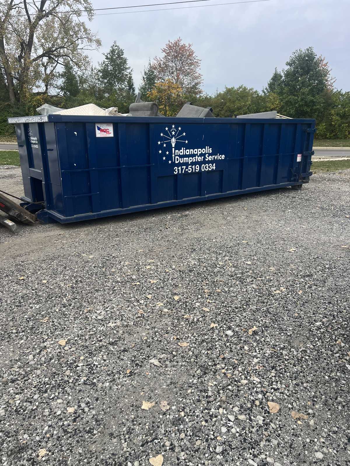 A navy Indianapolis Dumpster Service roll off container in Westfield. Loaded on a gravel lot, set on boards.
