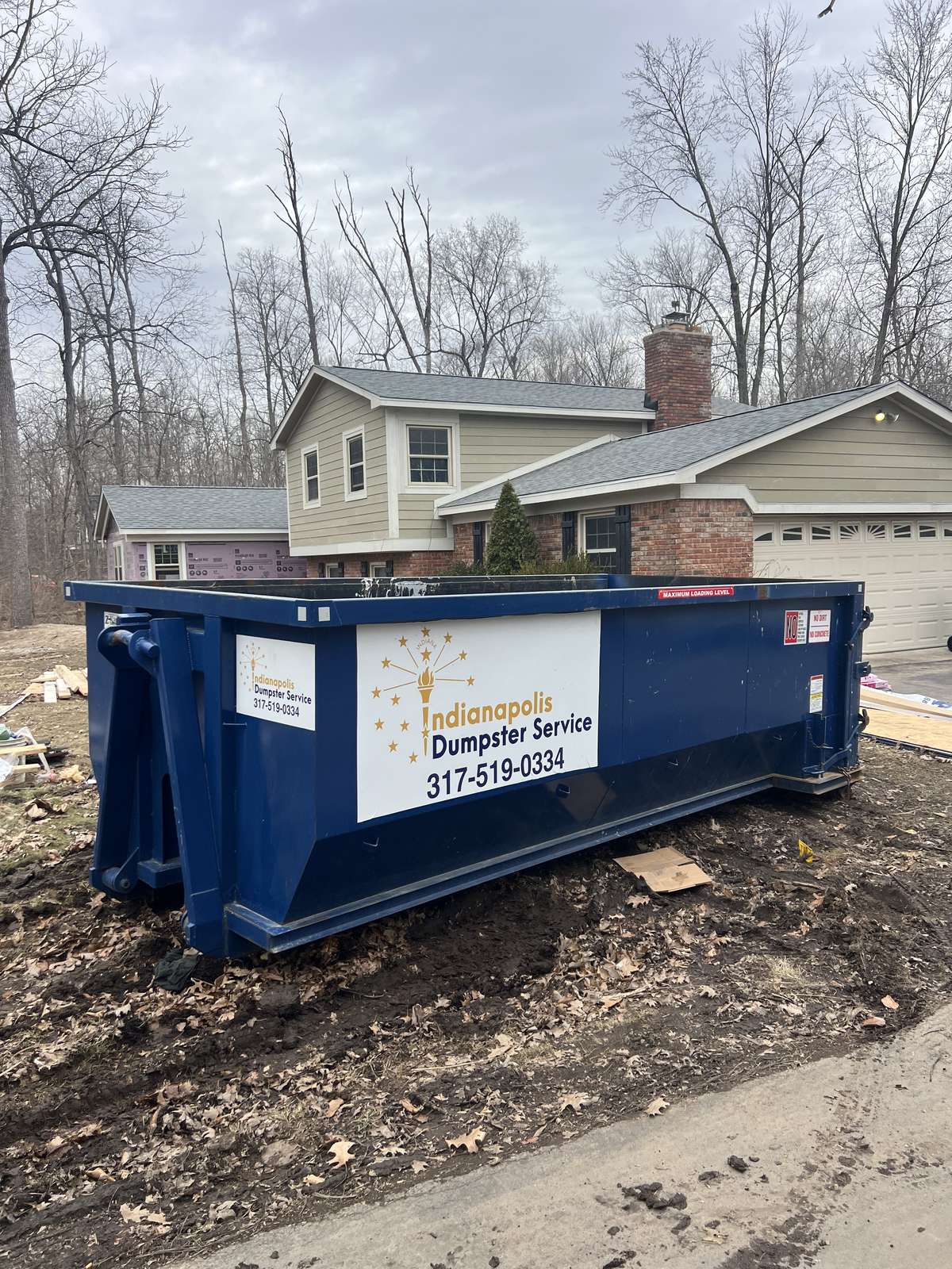 A navy Indianapolis Dumpster Service roll off container in Zionsville. On the driveway of a stone-front home.
