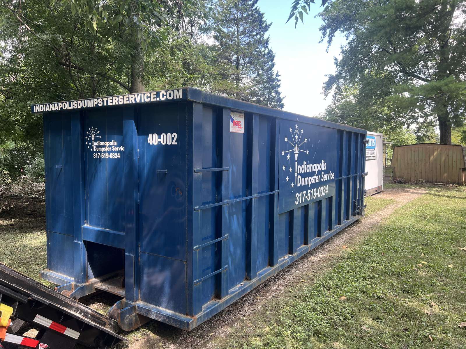 A navy Indianapolis Dumpster Service roll-off dumpster coming off our truck