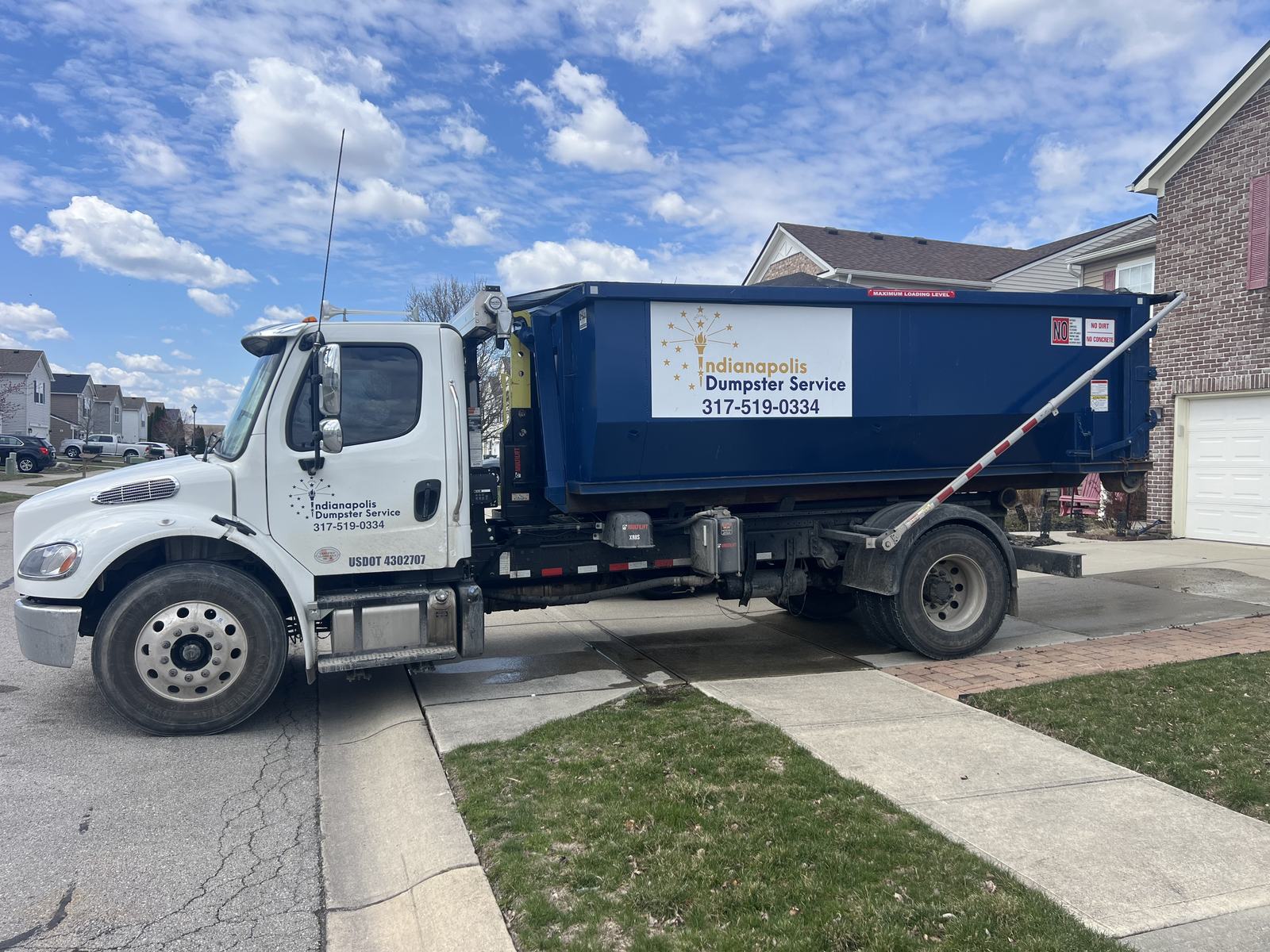 A navy Indianapolis Dumpster Service roll off container. Our truck carrying a dumpster in a residential driveway.